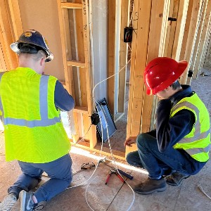Two students work at placing an electrical outlet in a new house.